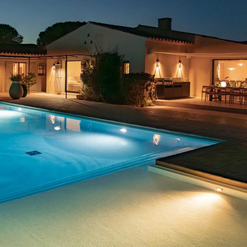Image d'une villa éclairée avec une piscine éclairée à la tombée de la nuit