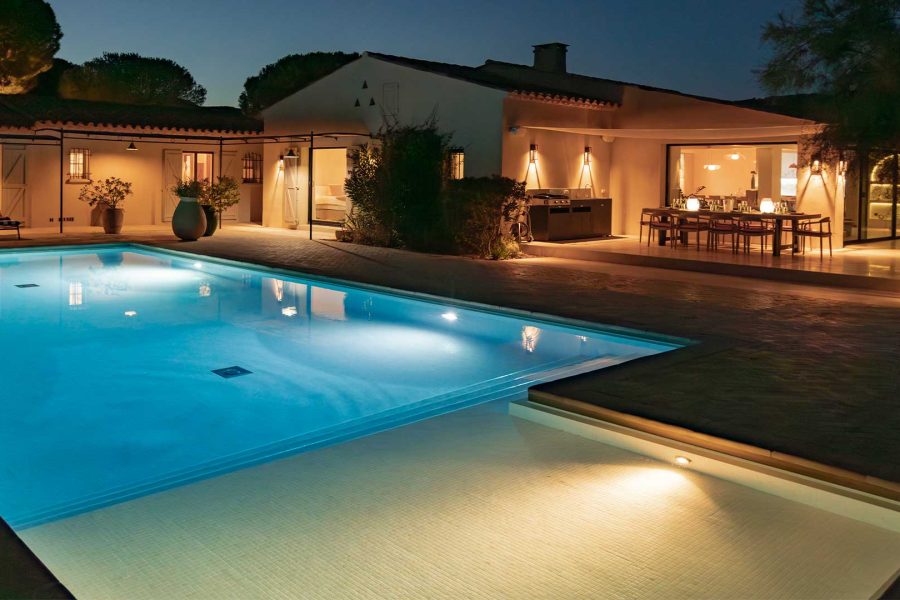 Image d'une villa éclairée avec une piscine éclairée à la tombée de la nuit